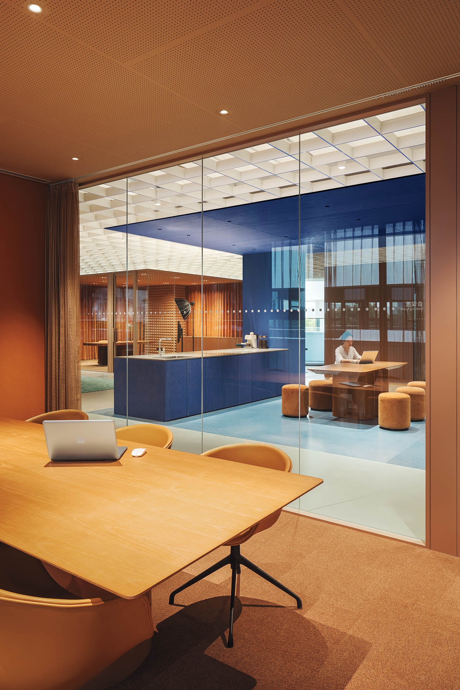 Stylish office with glass walls, featuring a wooden table with a laptop in the foreground