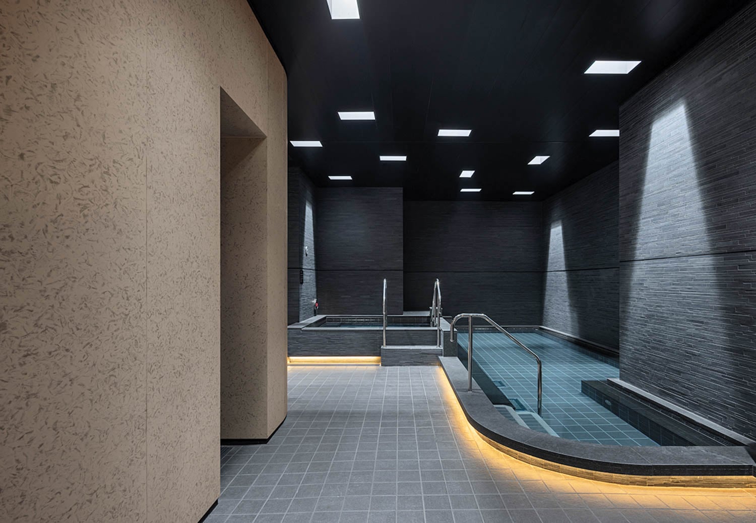 Modern indoor spa with large soaking pools and sleek stone walls. Soft lighting creates a calming, luxurious atmosphere
