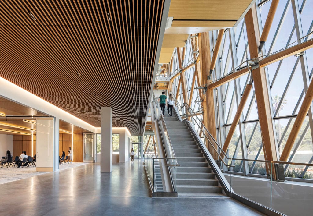 Modern atrium with wooden ceilings and glass walls, featuring a wide staircase