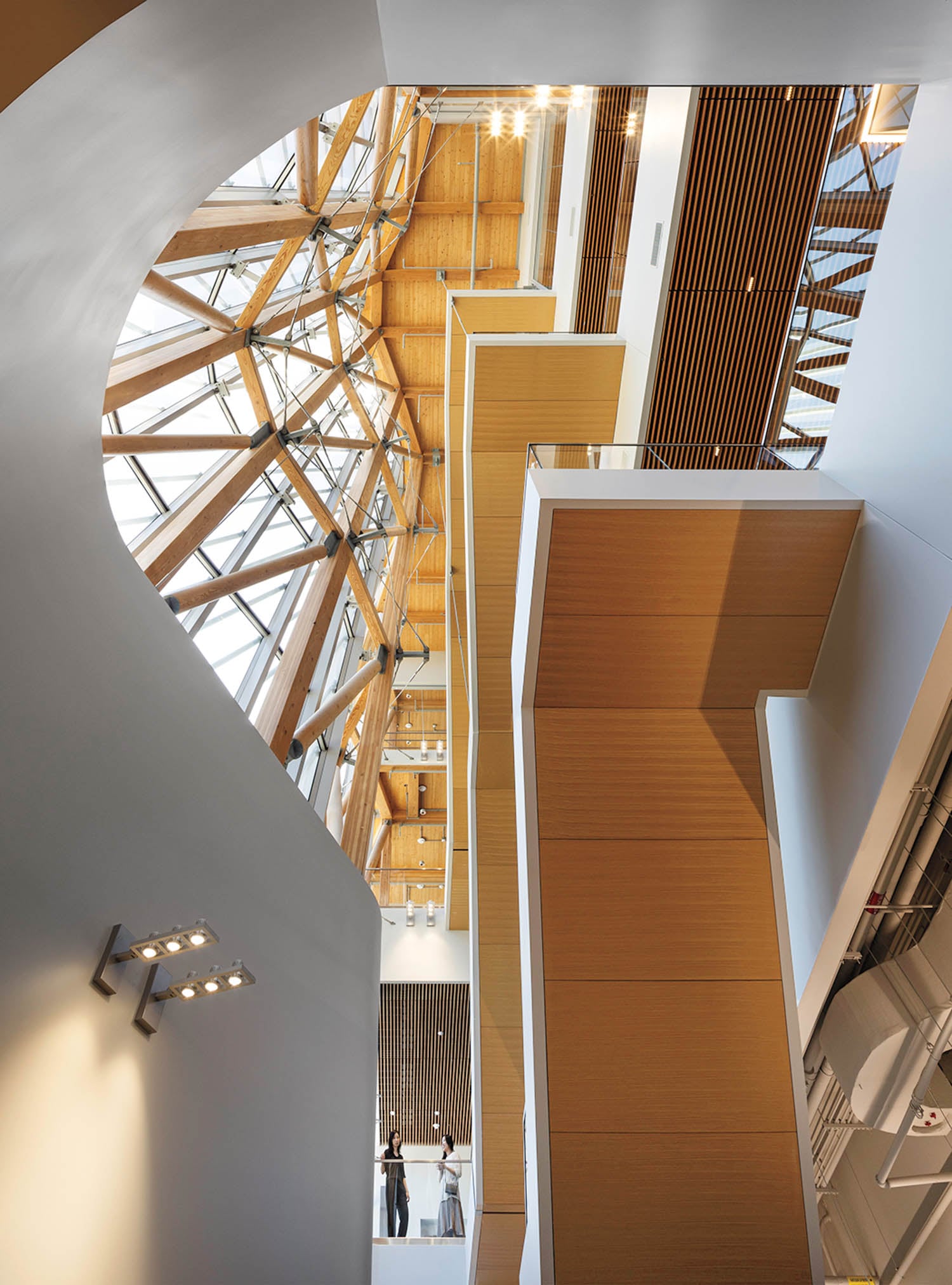 Spacious modern atrium with geometric wooden beams and large windows, bathing the space in natural light