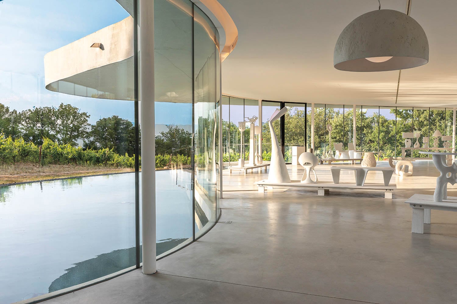 Modern interior with curved glass walls overlooking a serene pond and lush greenery
