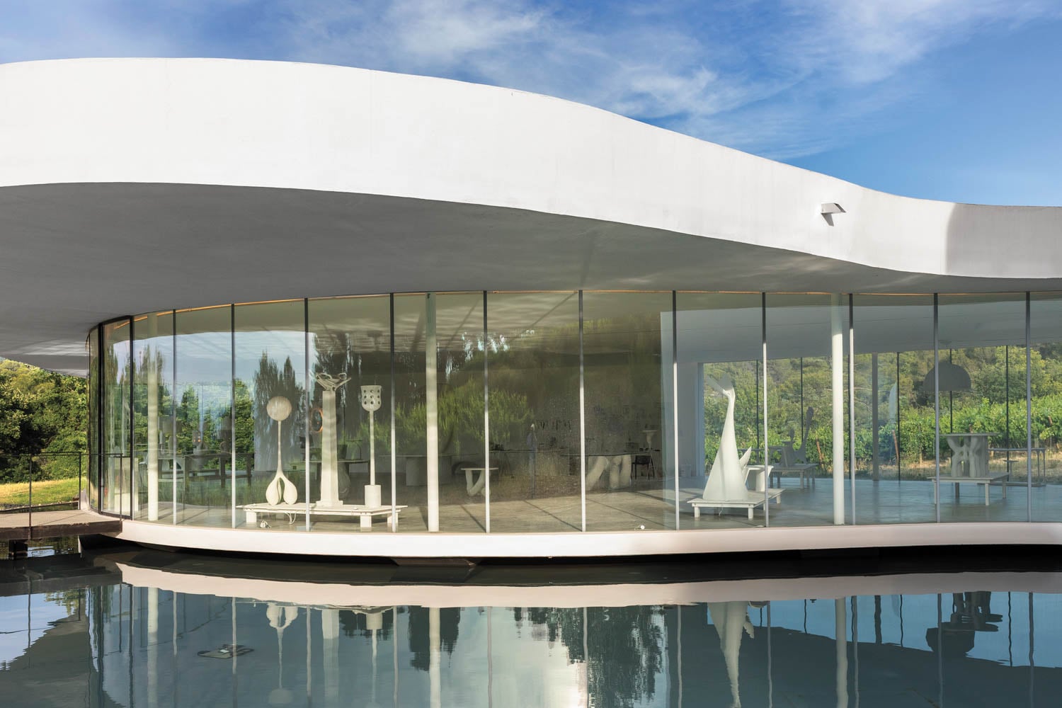 Modern glass building with a sleek, curved design reflecting in a calm water pool