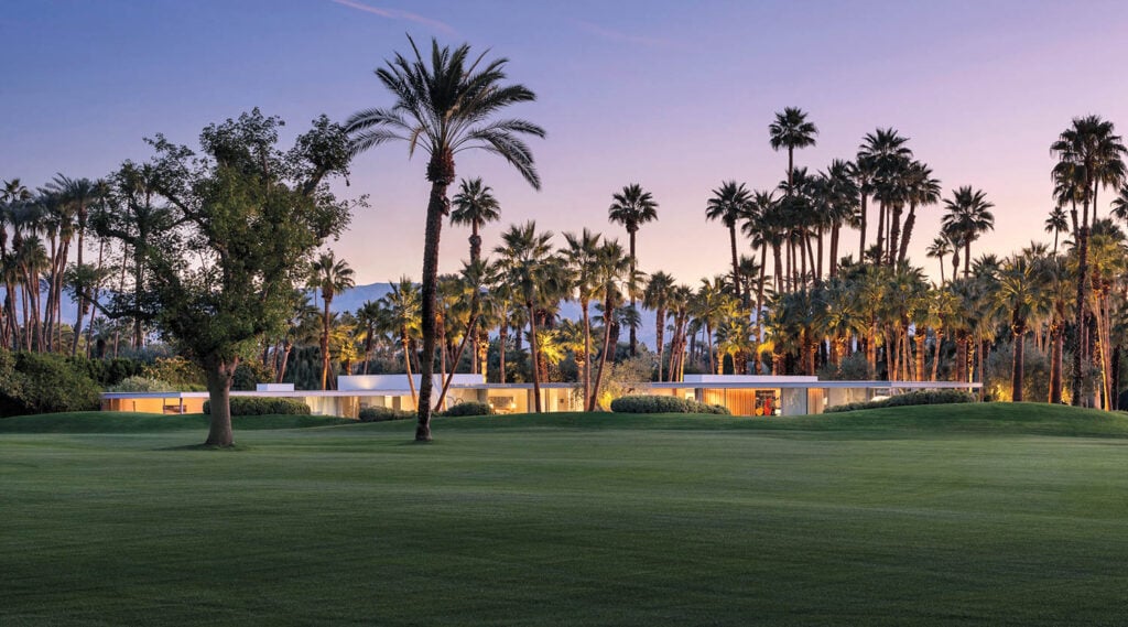 Modern house with large windows set amidst lush palm trees and green lawn at sunset