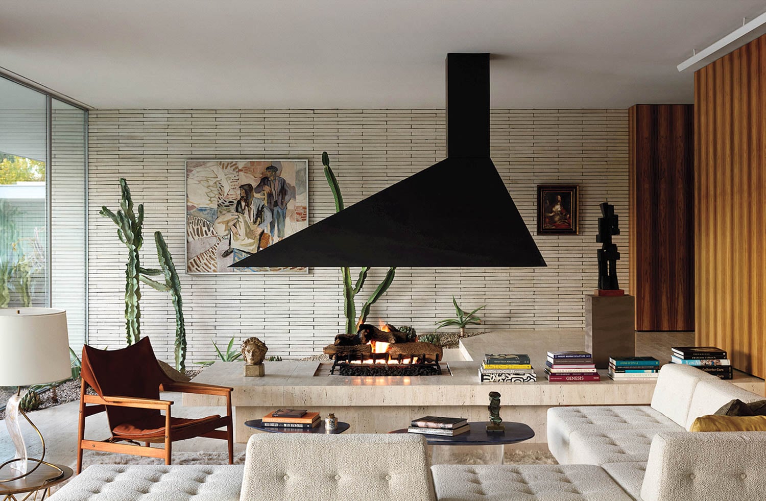 Modern living room with a central black fireplace, beige couches, and cactus plants