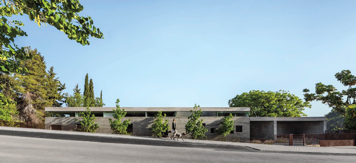 Single-story modern house with a flat roof and stone facade, surrounded by trees