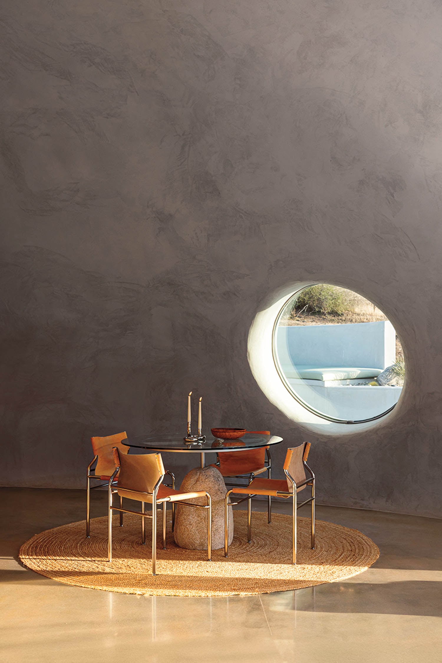 A minimalist dining area with a round black table, four leather chairs on a woven rug