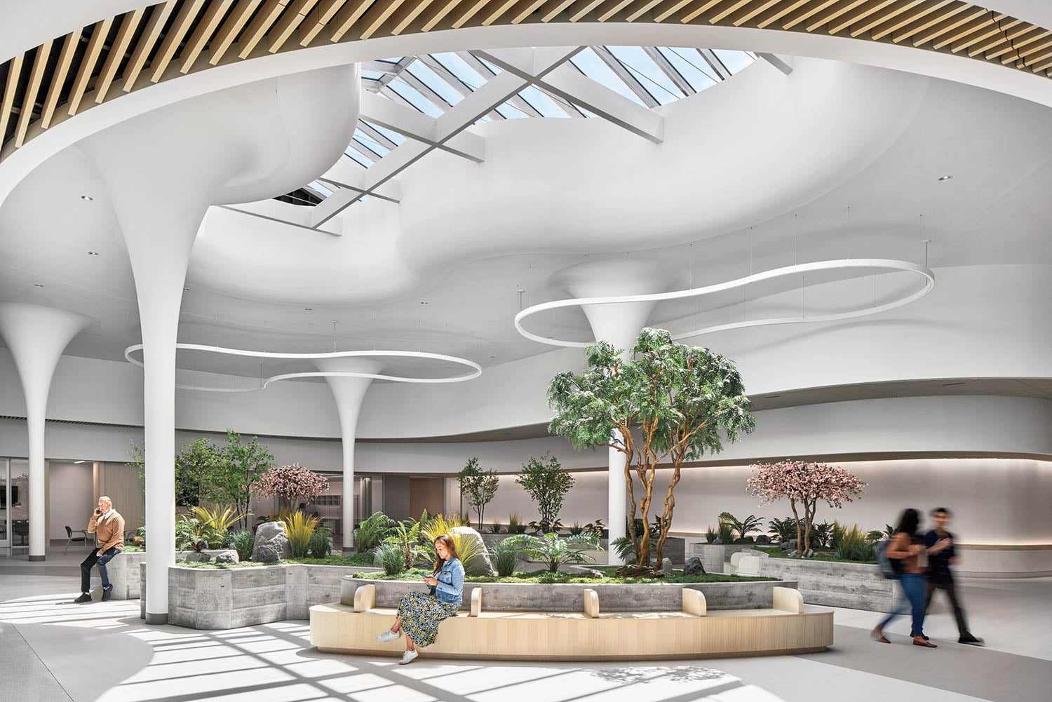 Modern indoor atrium with skylight, circular seating, and lush greenery