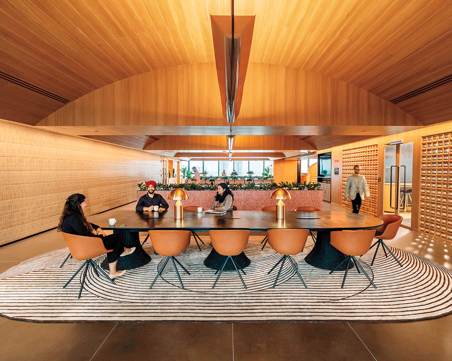 Modern office with wooden ceiling, large table surrounded by orange chairs on a striped rug