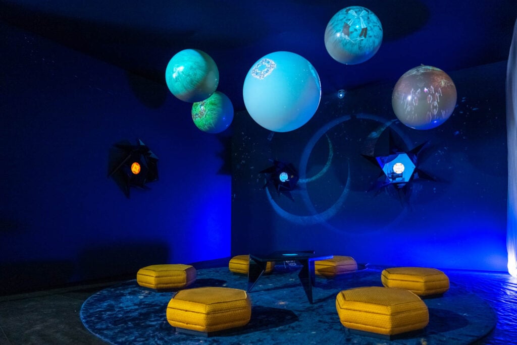 A dark, immersive room with glowing spheres resembling planets hanging from the ceiling