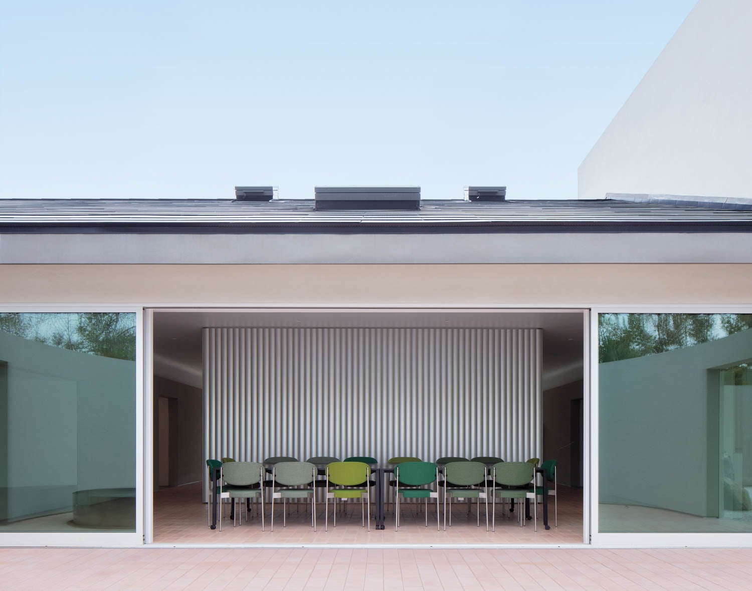 Modern architectural space with large glass doors revealing a row of green and gray chairs against a striped wall