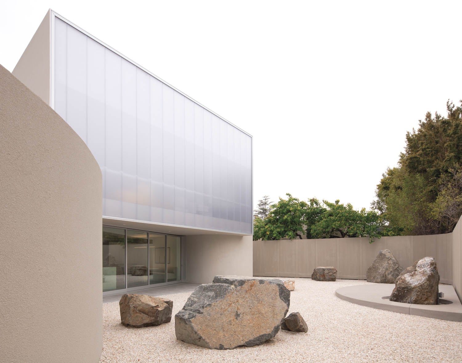 Modern minimalist courtyard with large rocks on gravel, surrounded by curved beige walls