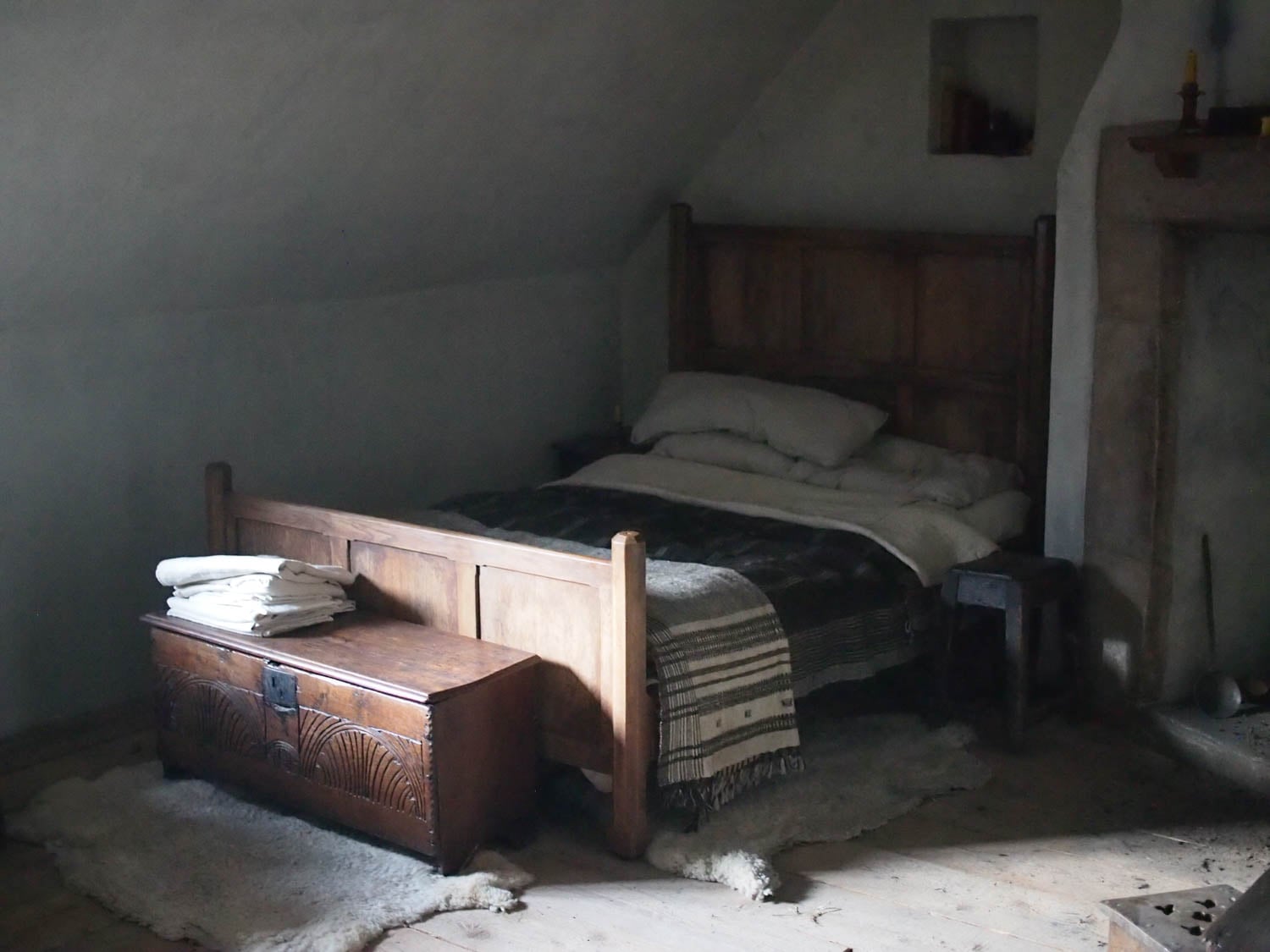 A dimly lit rustic bedroom with a wooden bed, plush pillows, and a wool blanket