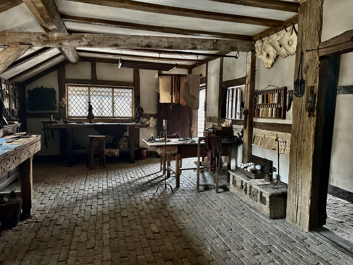 A rustic workshop with wooden beams, brick floor, and tools hanging on the walls