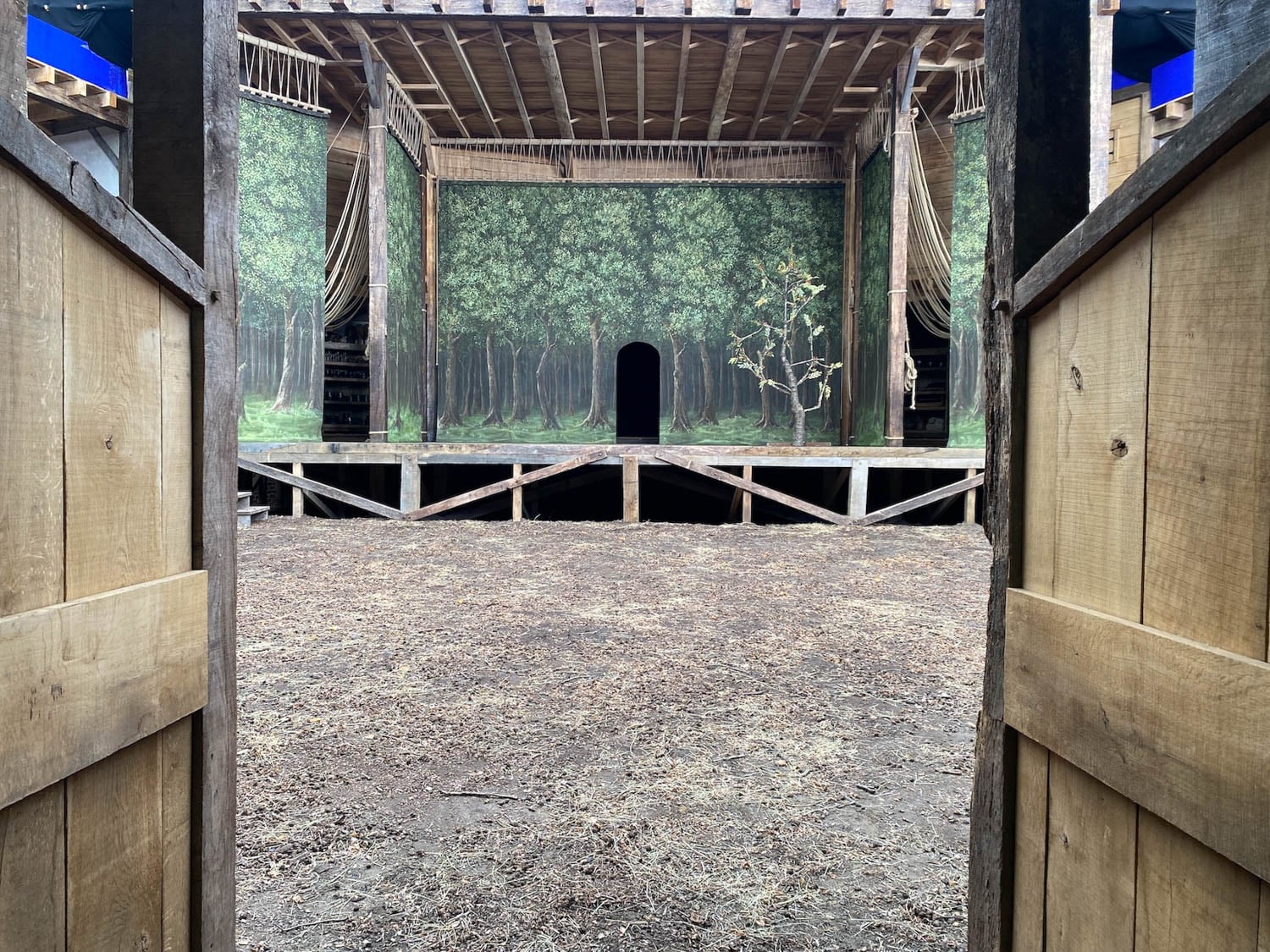 View of rustic theater stage through open wooden doors, depicting a forest backdrop with lush trees