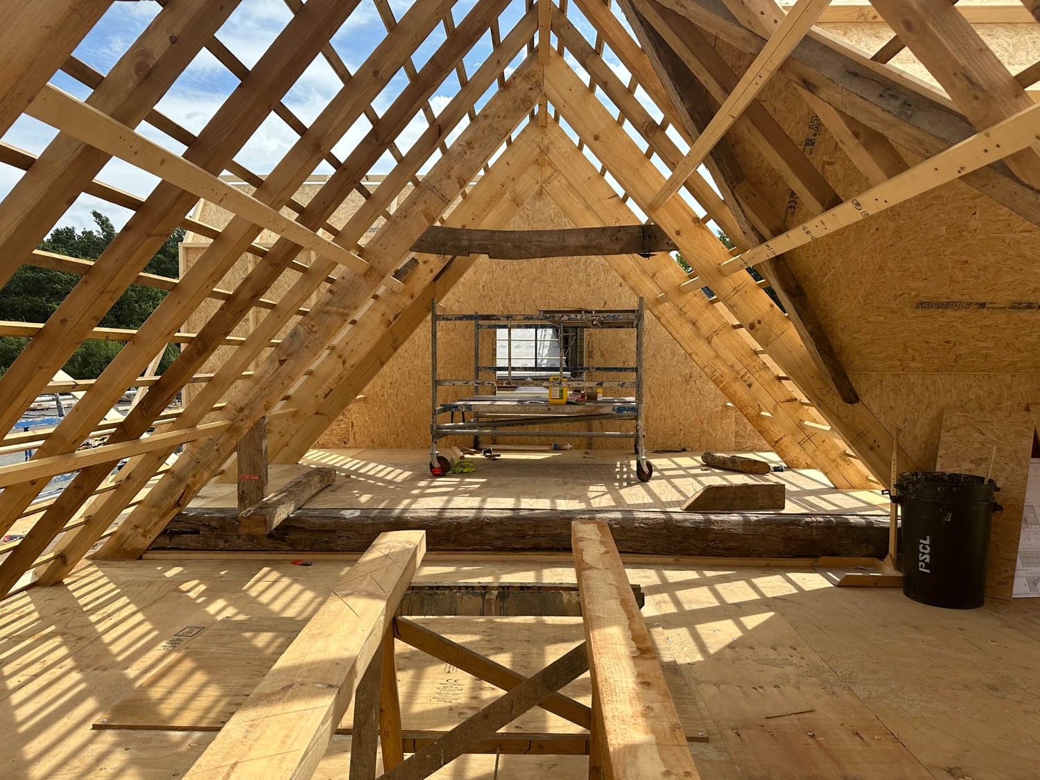 Wooden attic under construction with visible beams and trusses, sunlight casting shadows