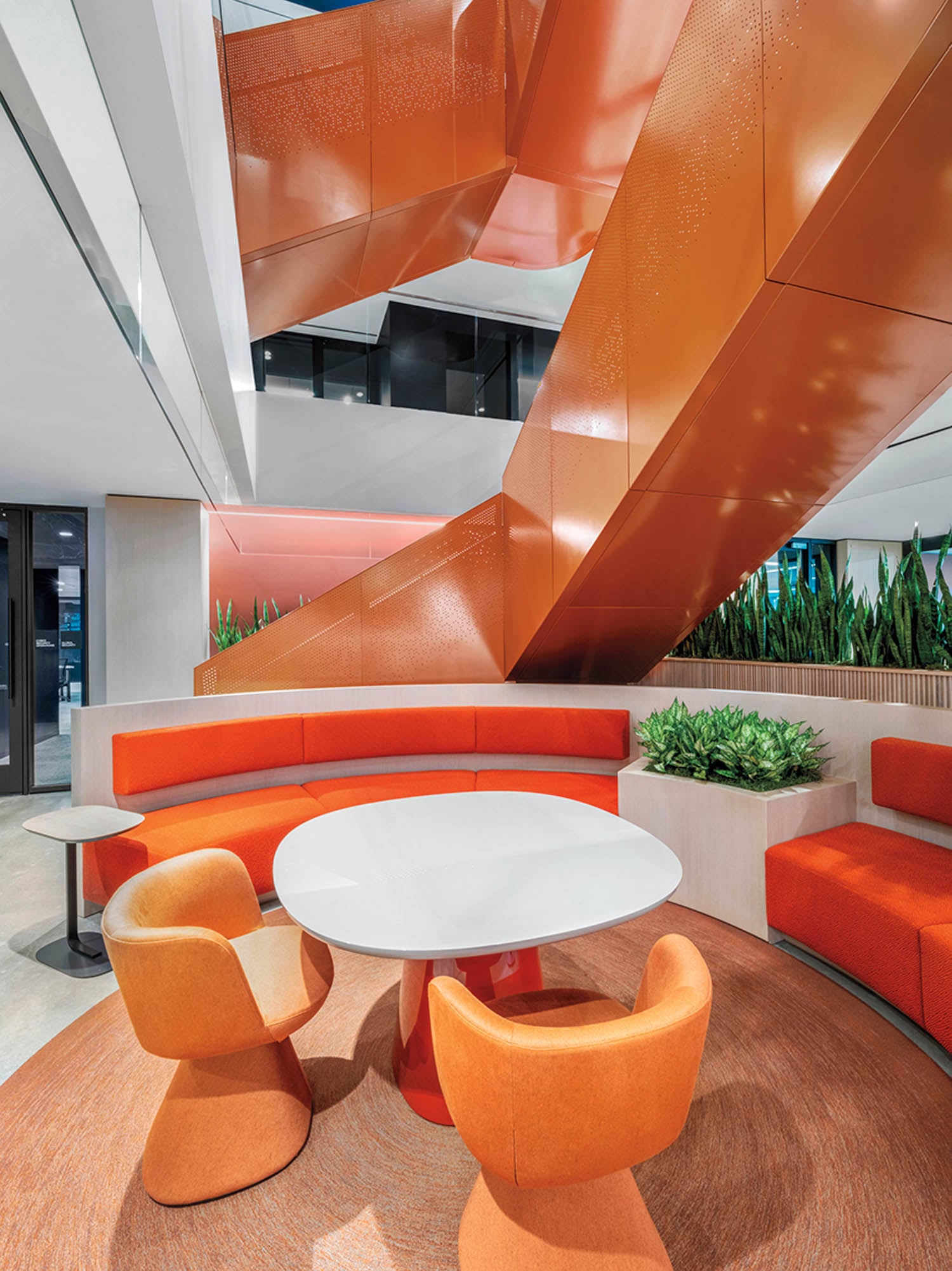 Modern lobby with vibrant orange accents, featuring a circular seating area, white round table, and orange spiral staircase