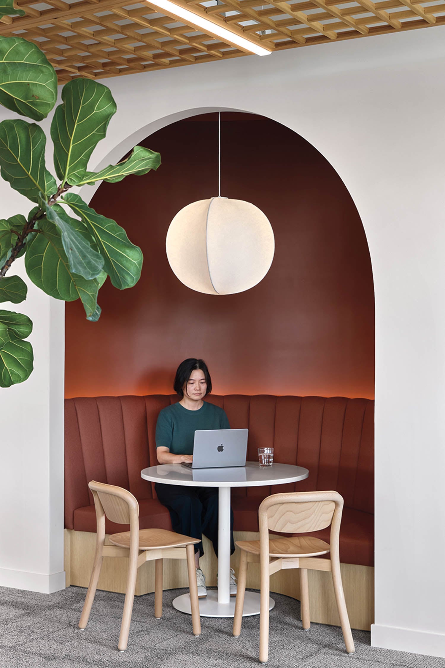 A person sits at a round table with a laptop in a stylish alcove with a brown cushioned booth