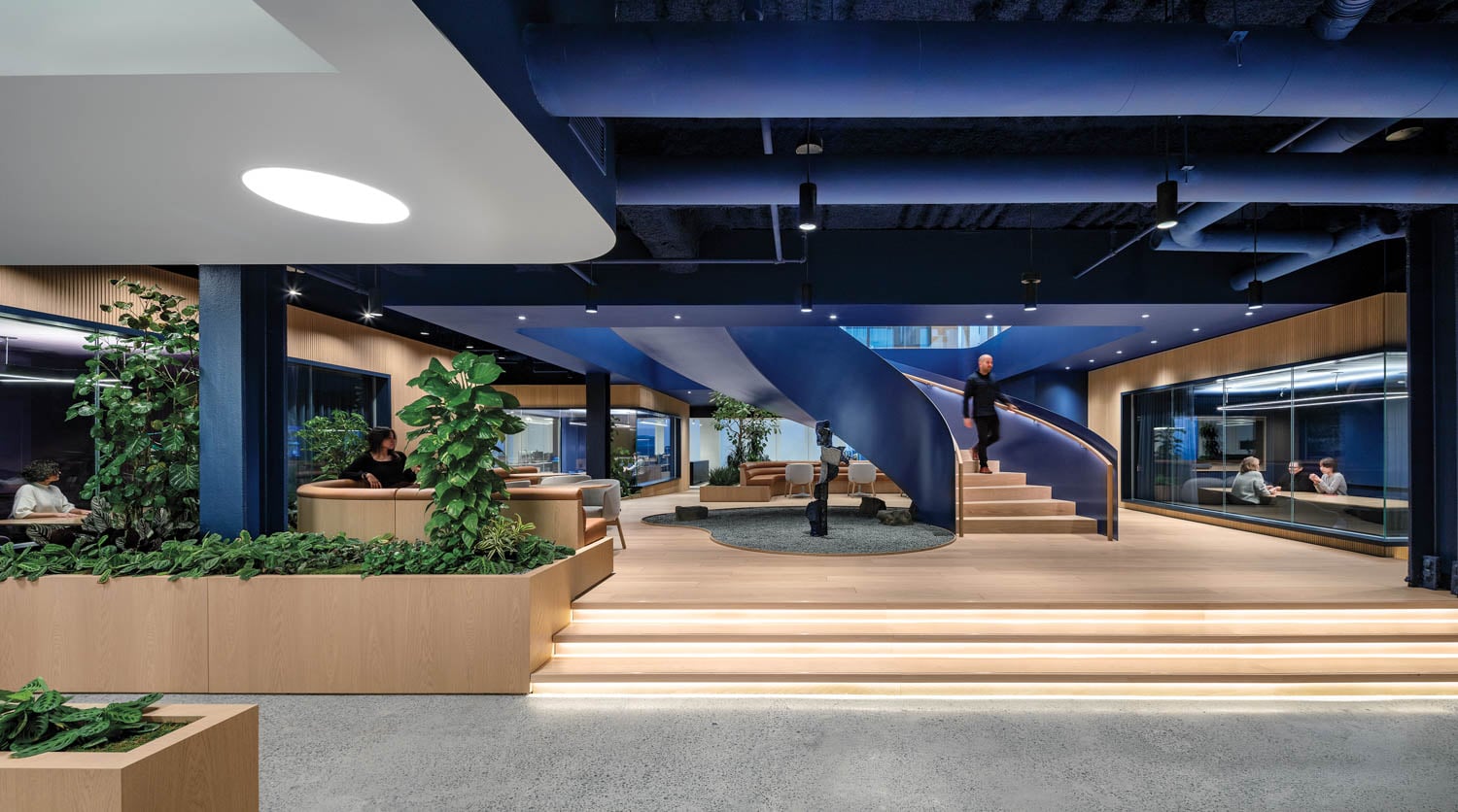 Modern office with a curved staircase, wooden seating areas, and green plants