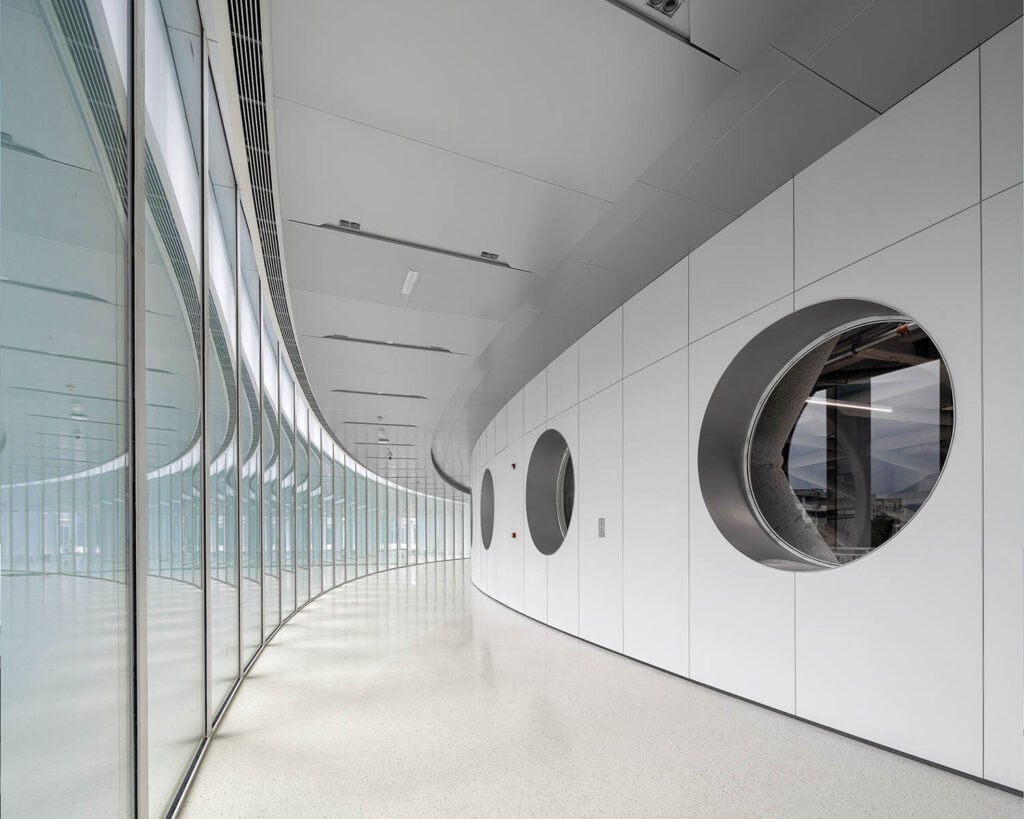 Modern corridor with curved glass walls on the left, reflecting light