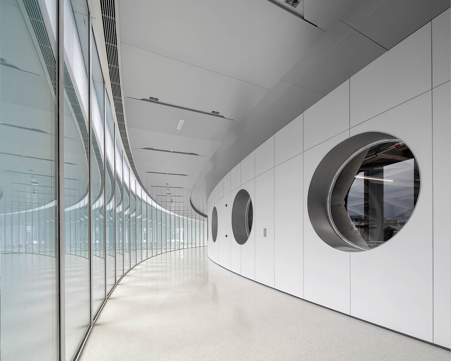 Modern corridor with curved glass walls on the left, reflecting light