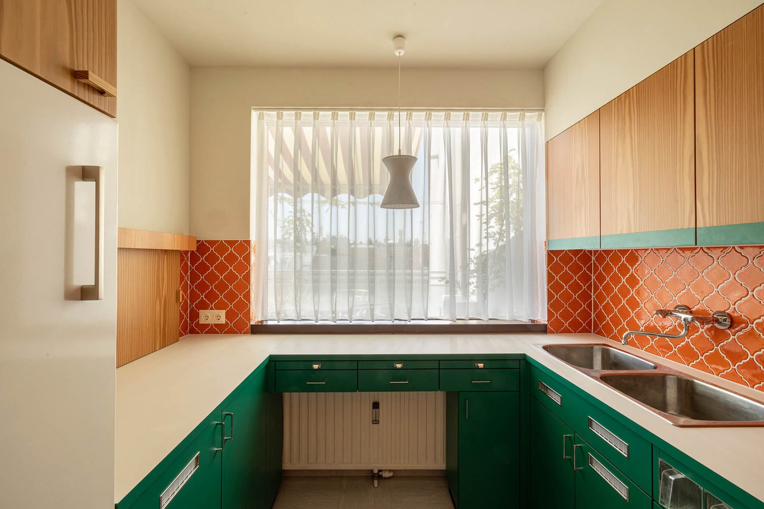kitchen with green cabinets and white curtains designed by Margarete Schütte-Lihotzky