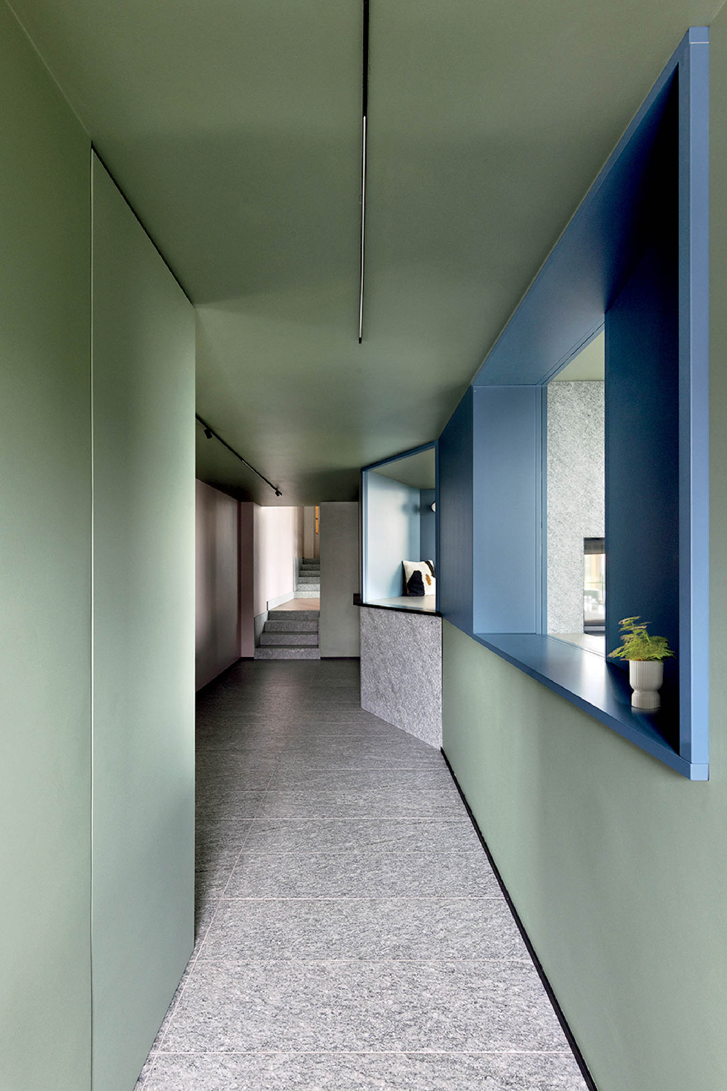 A long hallway with a blue door and a white wall.