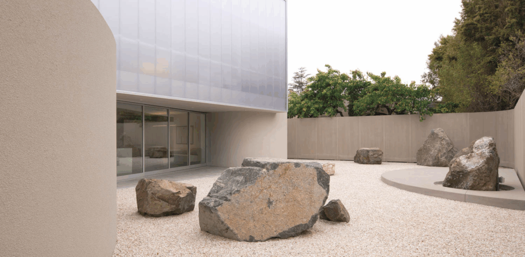 Modern minimalist courtyard with large rocks on gravel, surrounded by curved beige walls
