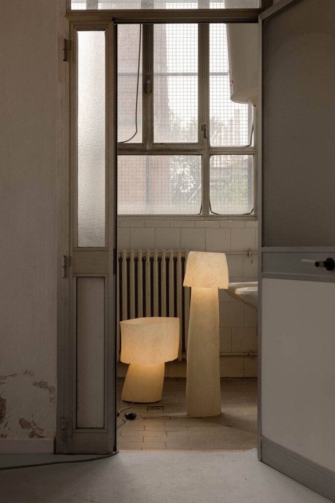 A small bathroom with frosted glass door, tiled walls, a radiator under a window, a sink, and two glowing lamp-shaped lights on the floor.