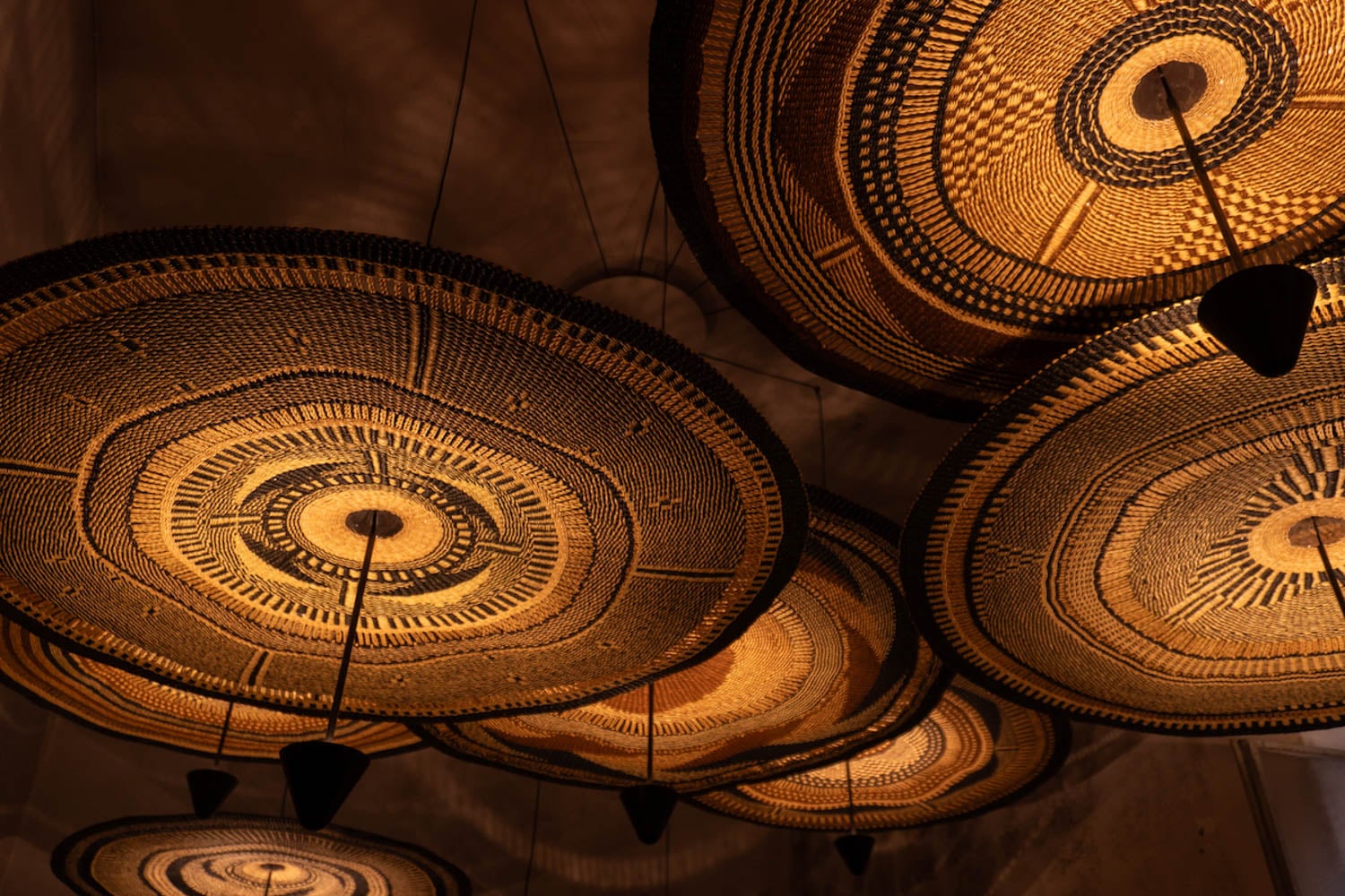 Close-up view of several woven basket-style ceiling lamps with warm lighting, casting patterned shadows on the ceiling.