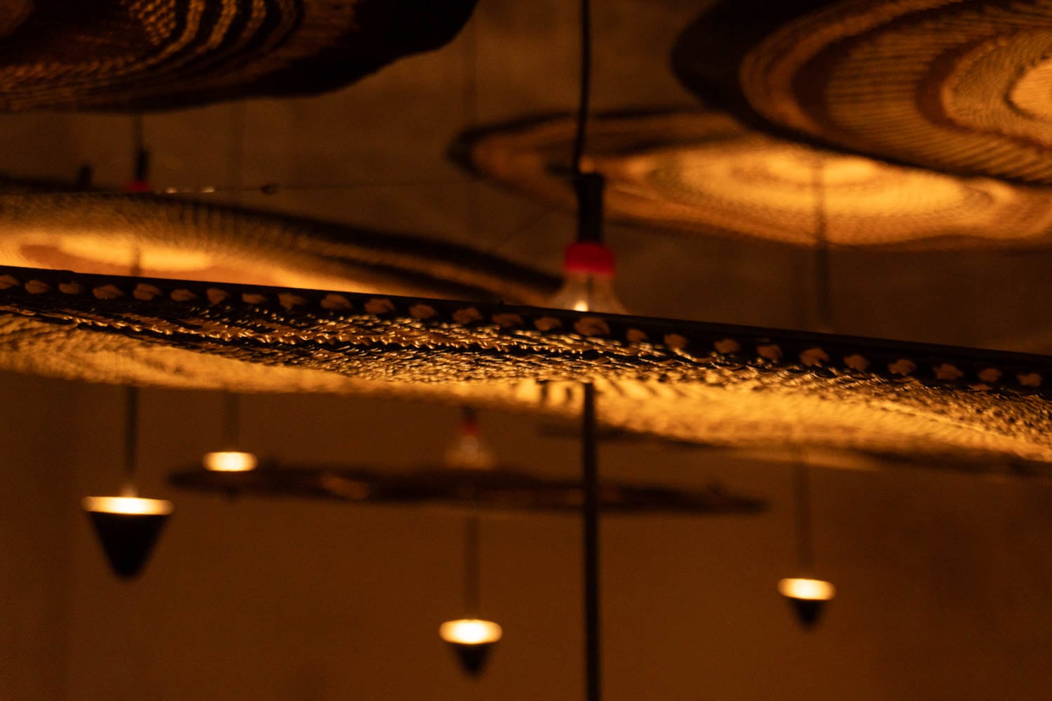Close-up of woven basket-like objects suspended from the ceiling with warm light bulbs illuminating them from above and below.