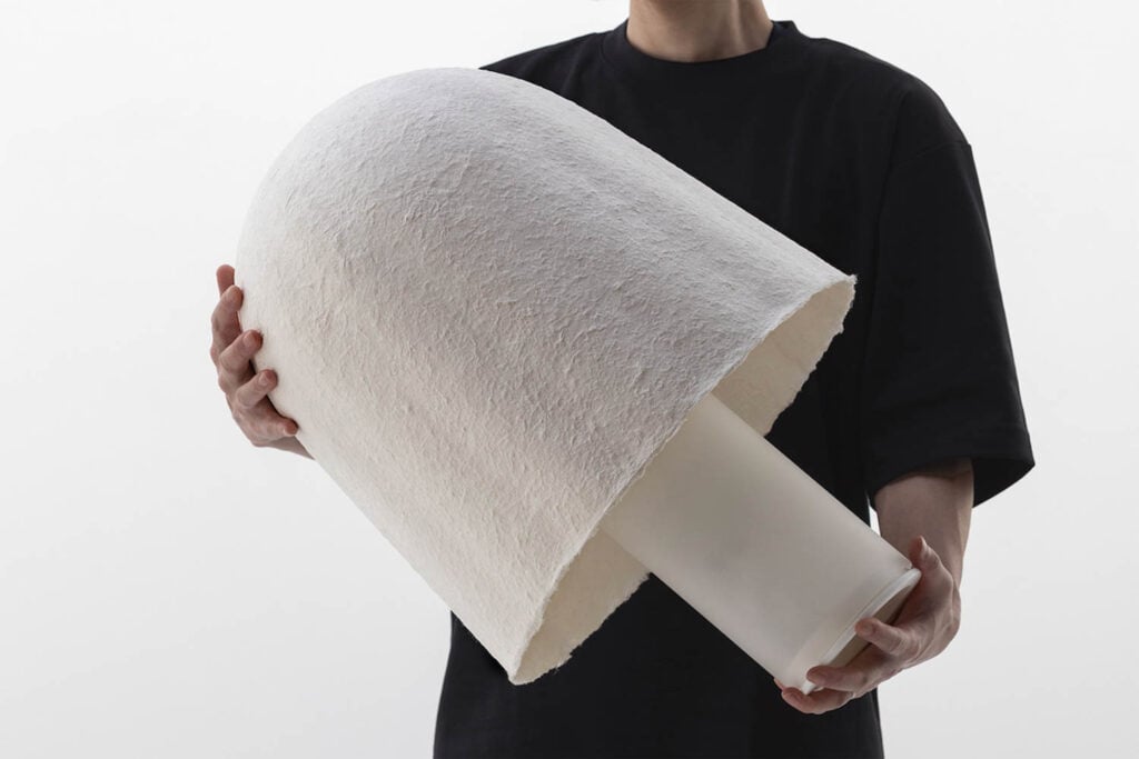 A person holding a large, dome-shaped white object with a cylindrical base against a plain background.