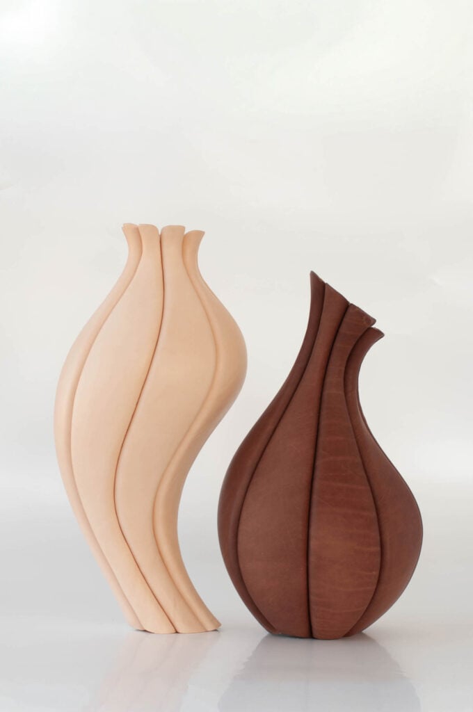 Two sculptural vases with smooth, undulating, organic curves stand side by side; one is light beige and the other is a rich brown color.