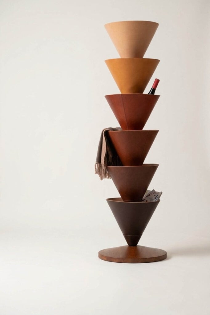 A vertical stack of six cone-shaped wooden bowls on a round base, with some holding a scarf, a bottle, and a rolled-up magazine, against a plain background.