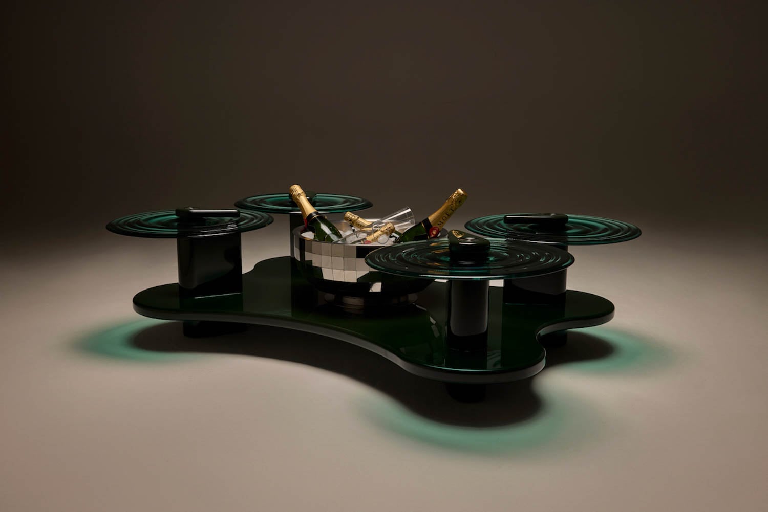 A modern black coffee table with four round glass surfaces and a mirrored ice bucket holding champagne bottles in the center.
