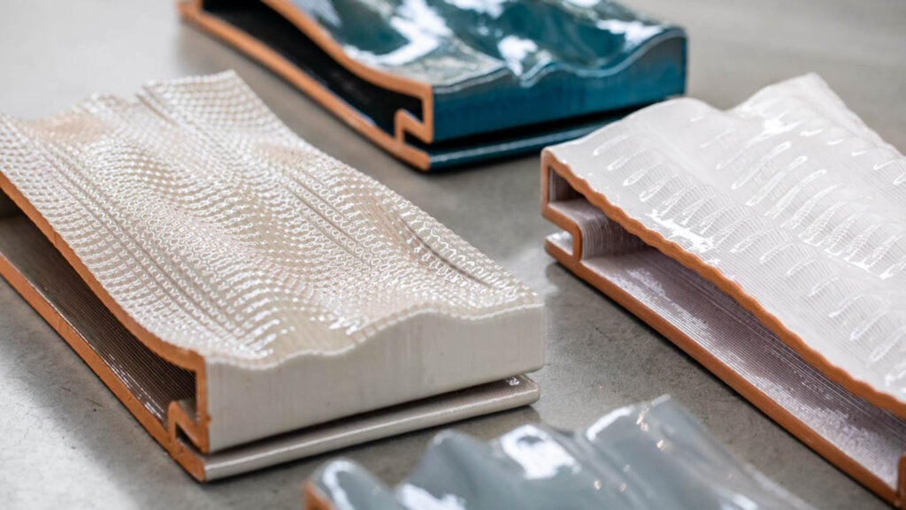 Four rectangular ceramic tiles with textured, wavy surfaces and glossy finishes are displayed on a flat surface. Each tile features a different color and pattern.