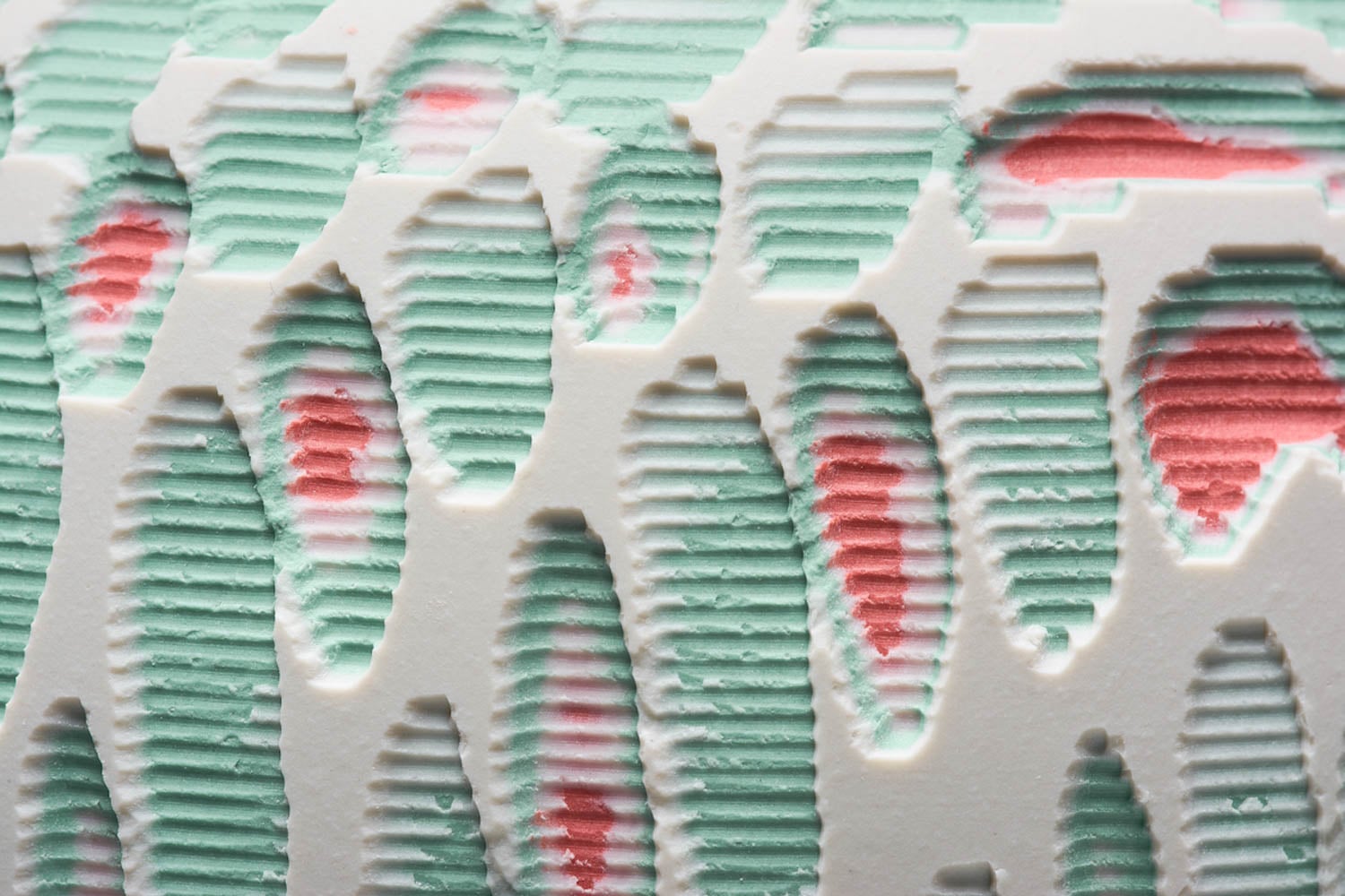 Close-up of a textured surface with layered, oval-shaped cutouts revealing green and pink colors beneath a white top layer.