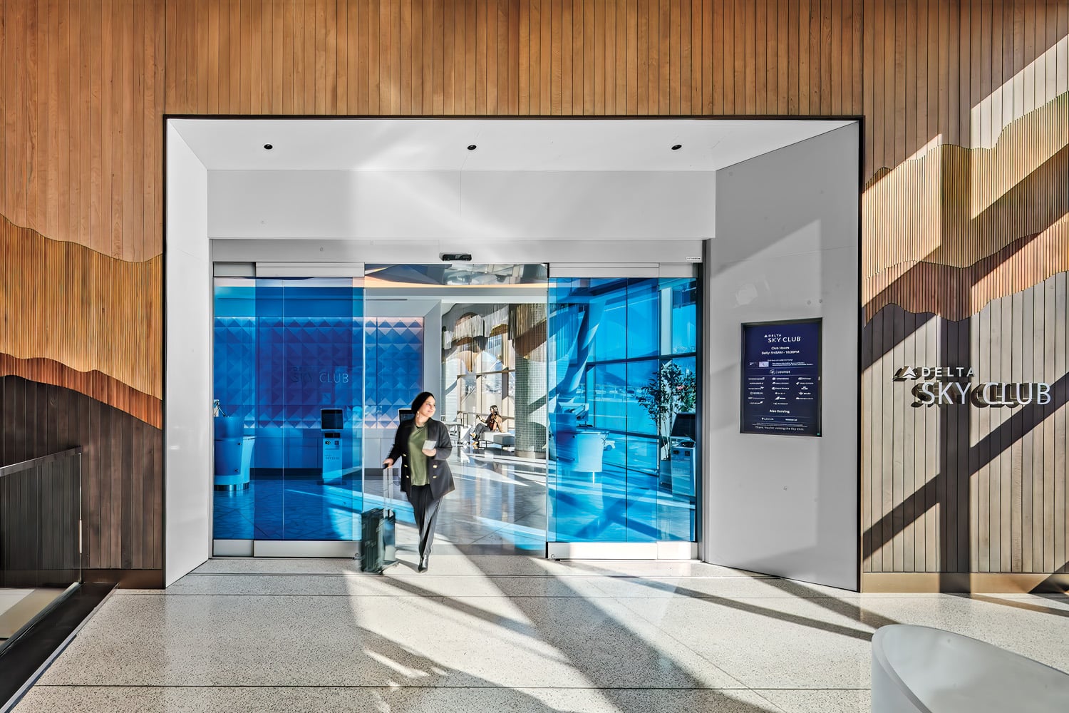 Walnut tambour paneling and Delta blue–tinted glass sliding doors mark the entry to the club