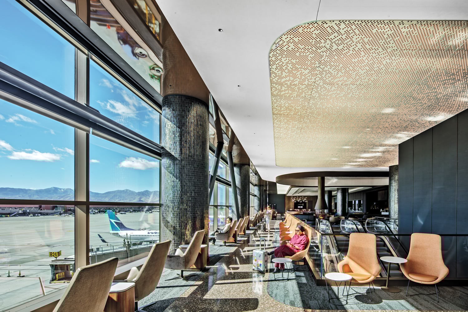 Poured terrazzo flooring in the earthy colors of a hiking trail leads guests through the lounge, where Paul Brayton Designs Ellary lounge chairs line the 15-foot-high window wall overlooking the tarmac and Oquirrh Mountains.