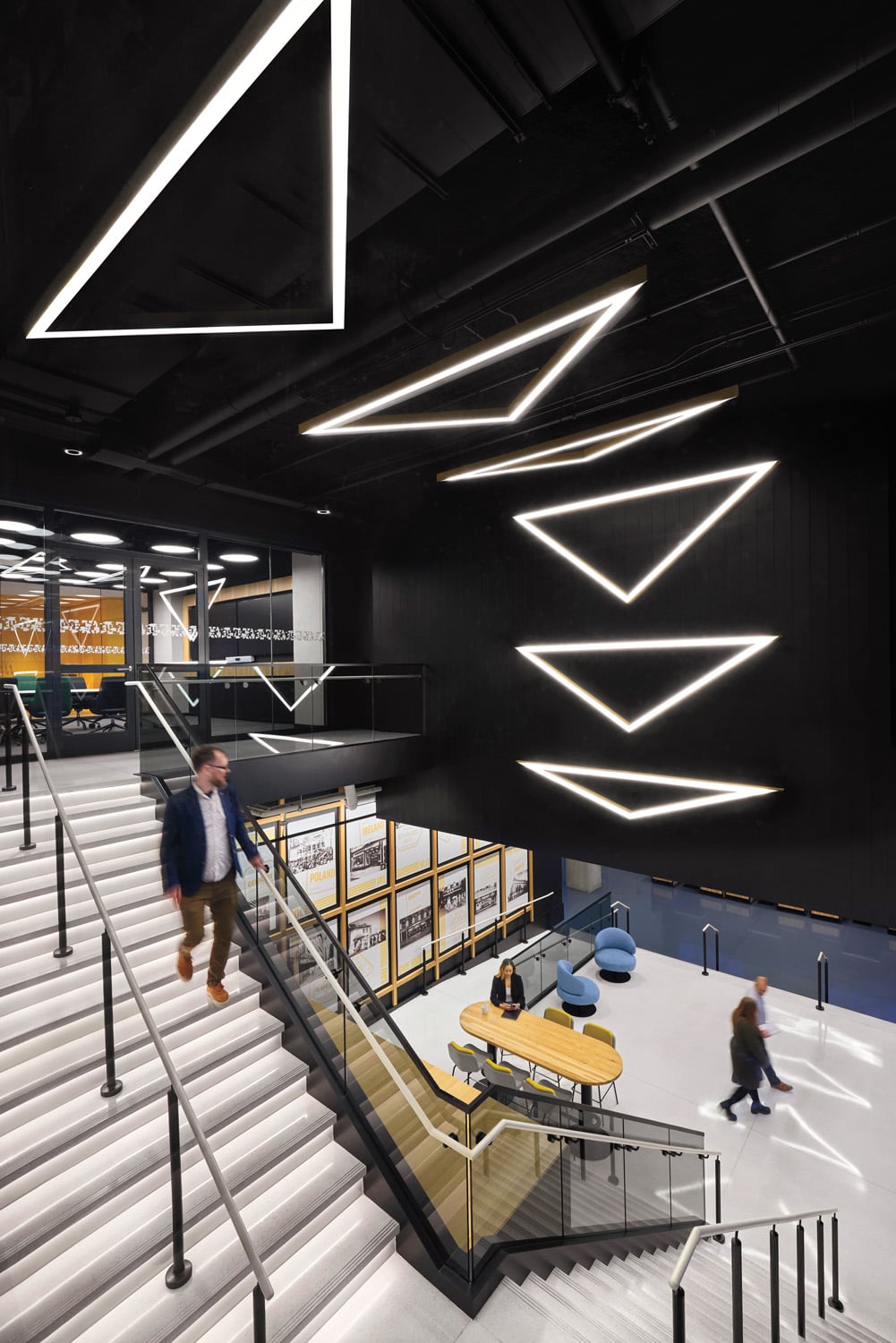 a staircase under a ceiling installation of neon triangles