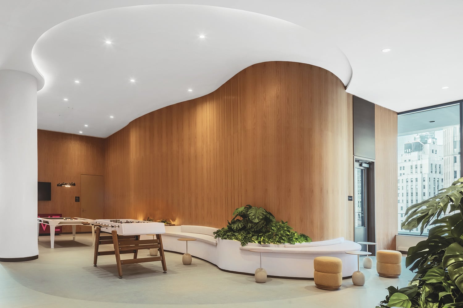 Modern office lounge with curved wood-paneled walls, white curved seating, green plants, small stools, and large windows showing city buildings.