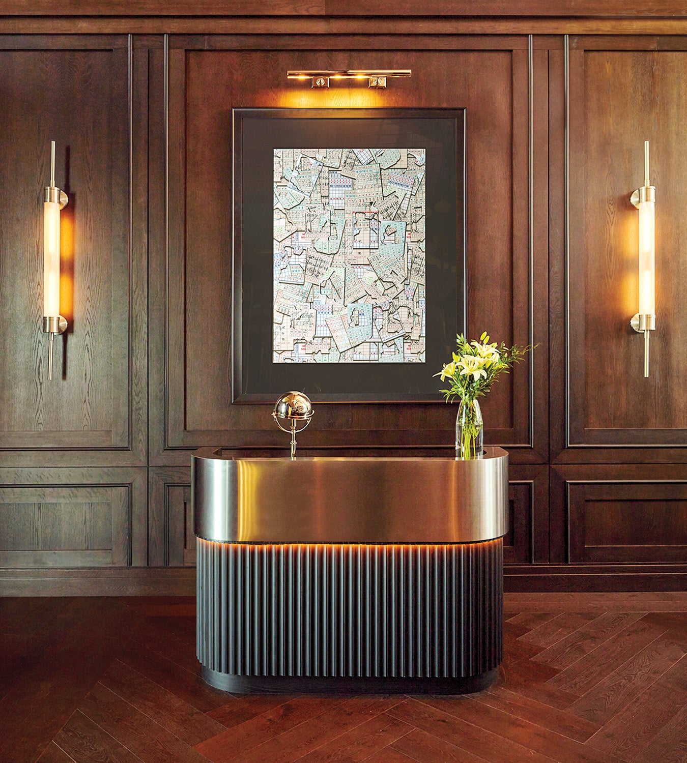 A modern bathroom vanity with a round mirror, vase of flowers, and metallic sink set against dark wood paneled walls and ambient wall sconces.