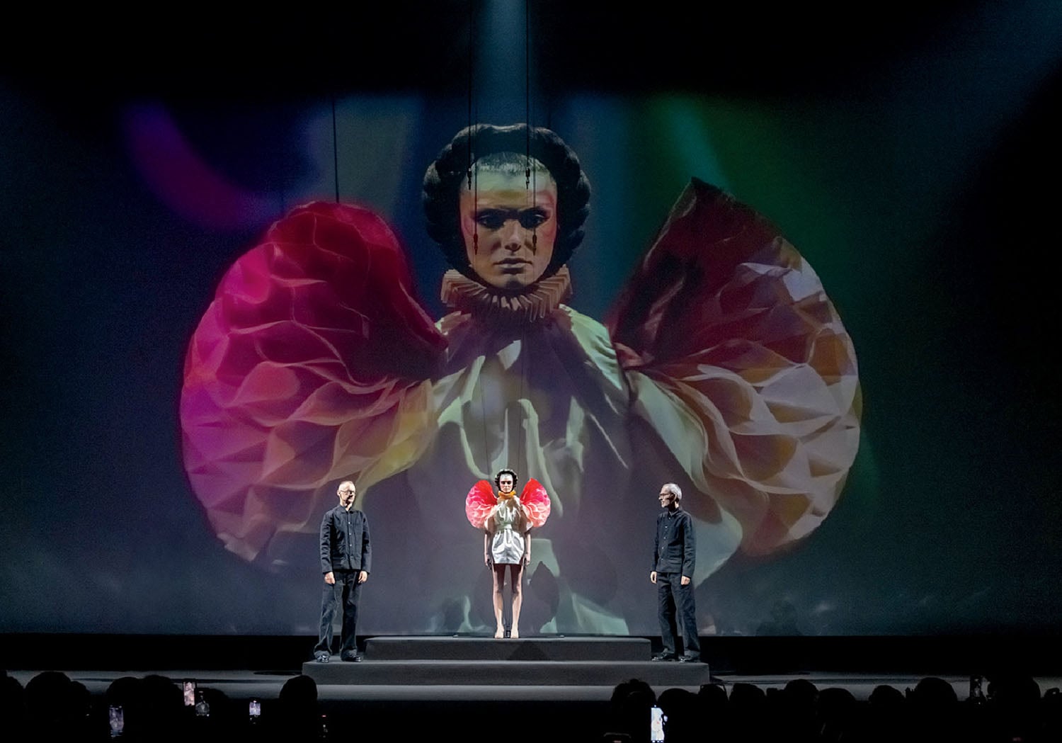 A couple of people on a stage with a large screen.