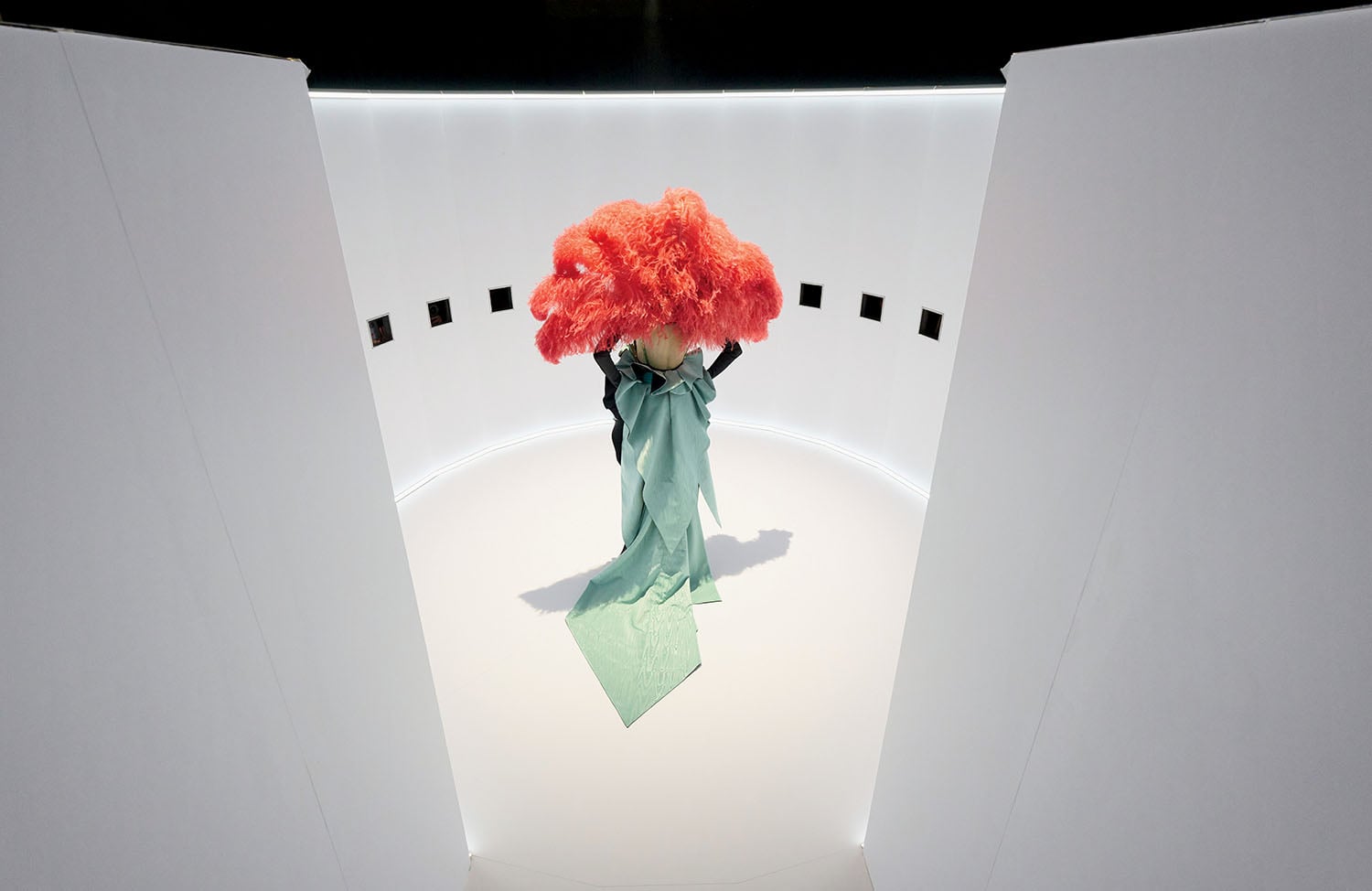 A woman with a red wig is standing in a white room.