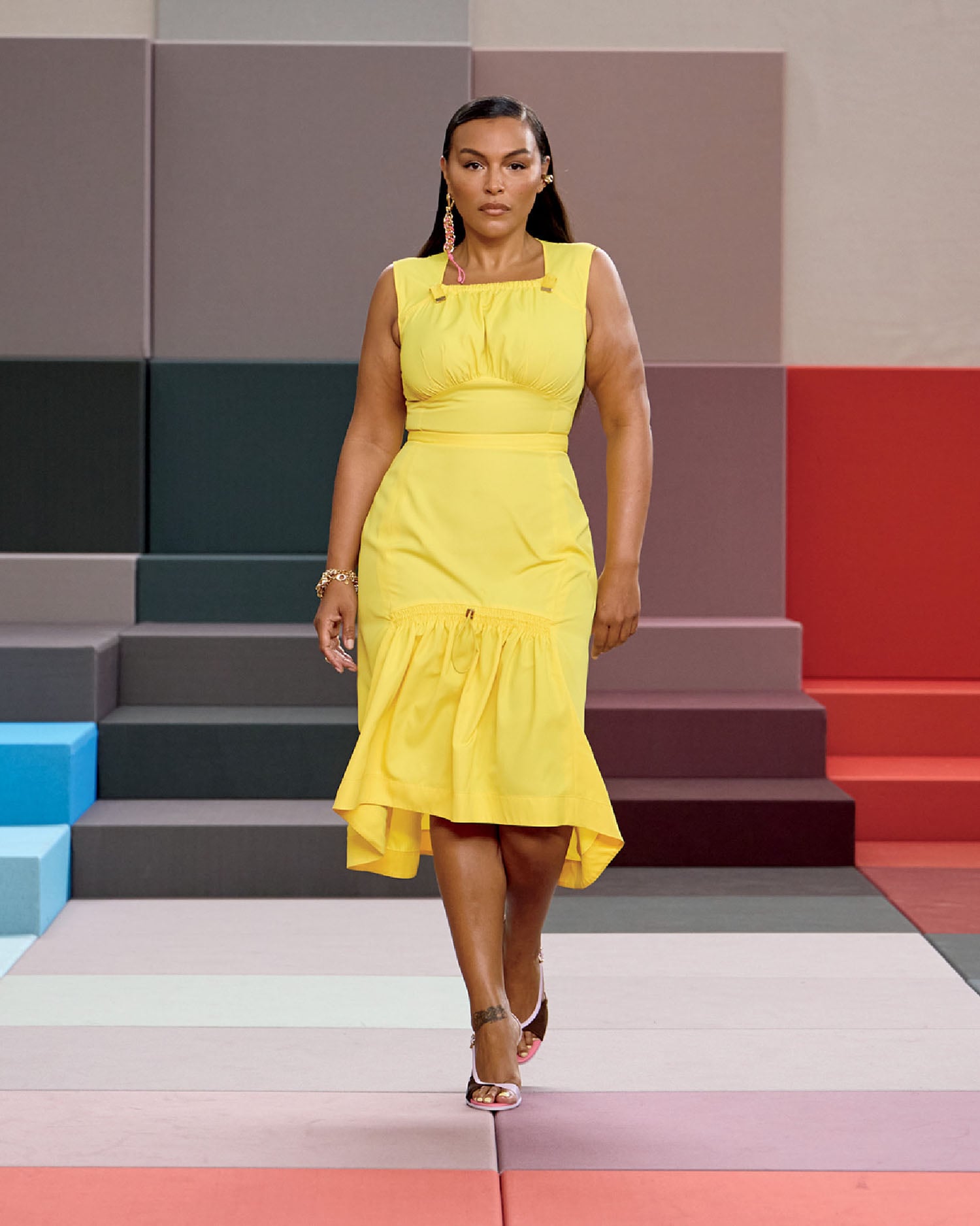 A woman in a yellow dress walks down a runway.