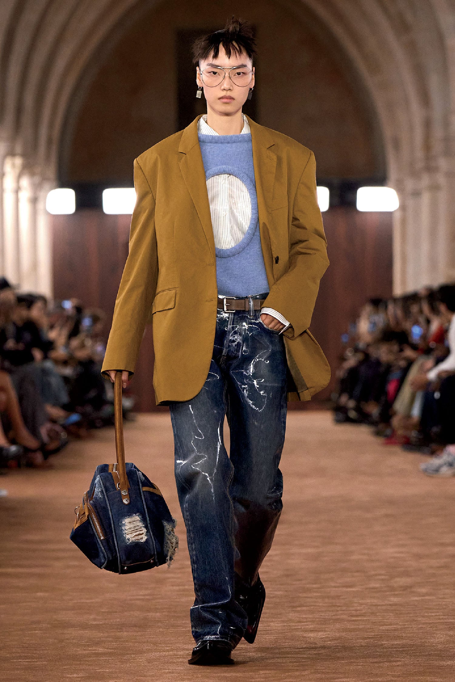 A model walks down the runway wearing a mustard colored jacket a.