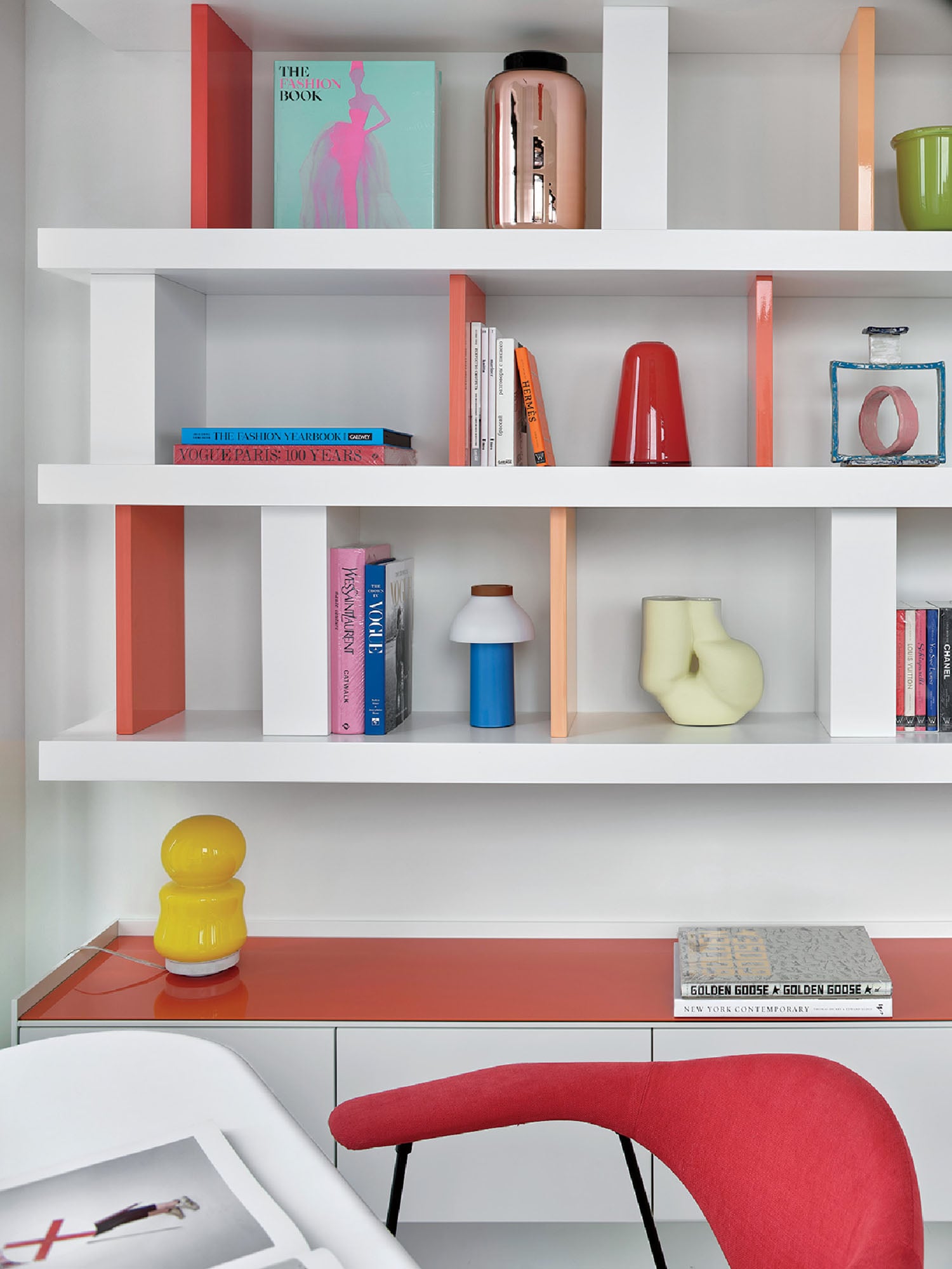 A desk with a red chair and a white shelf.