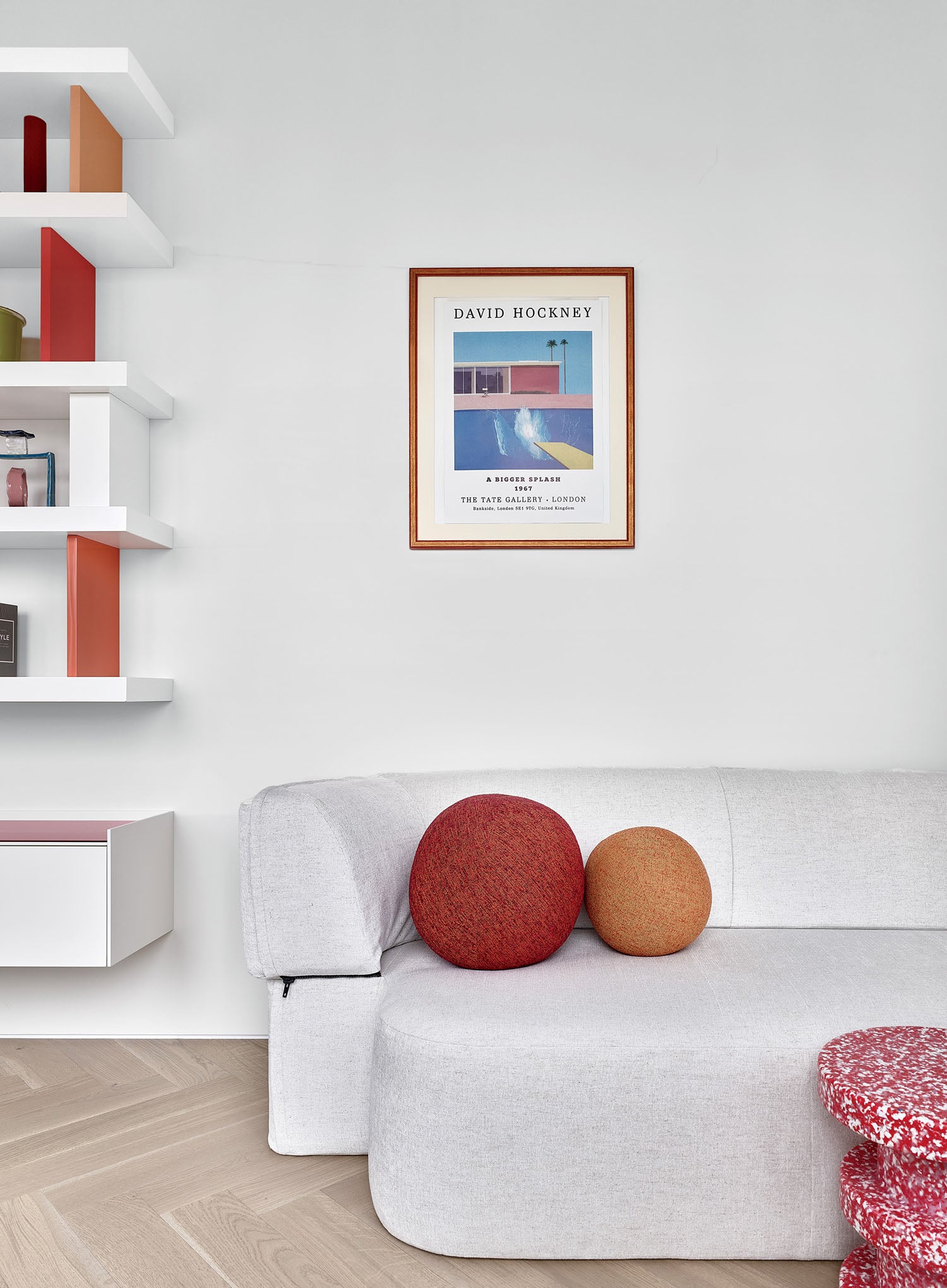 A white couch with a red pillow and a white wall.