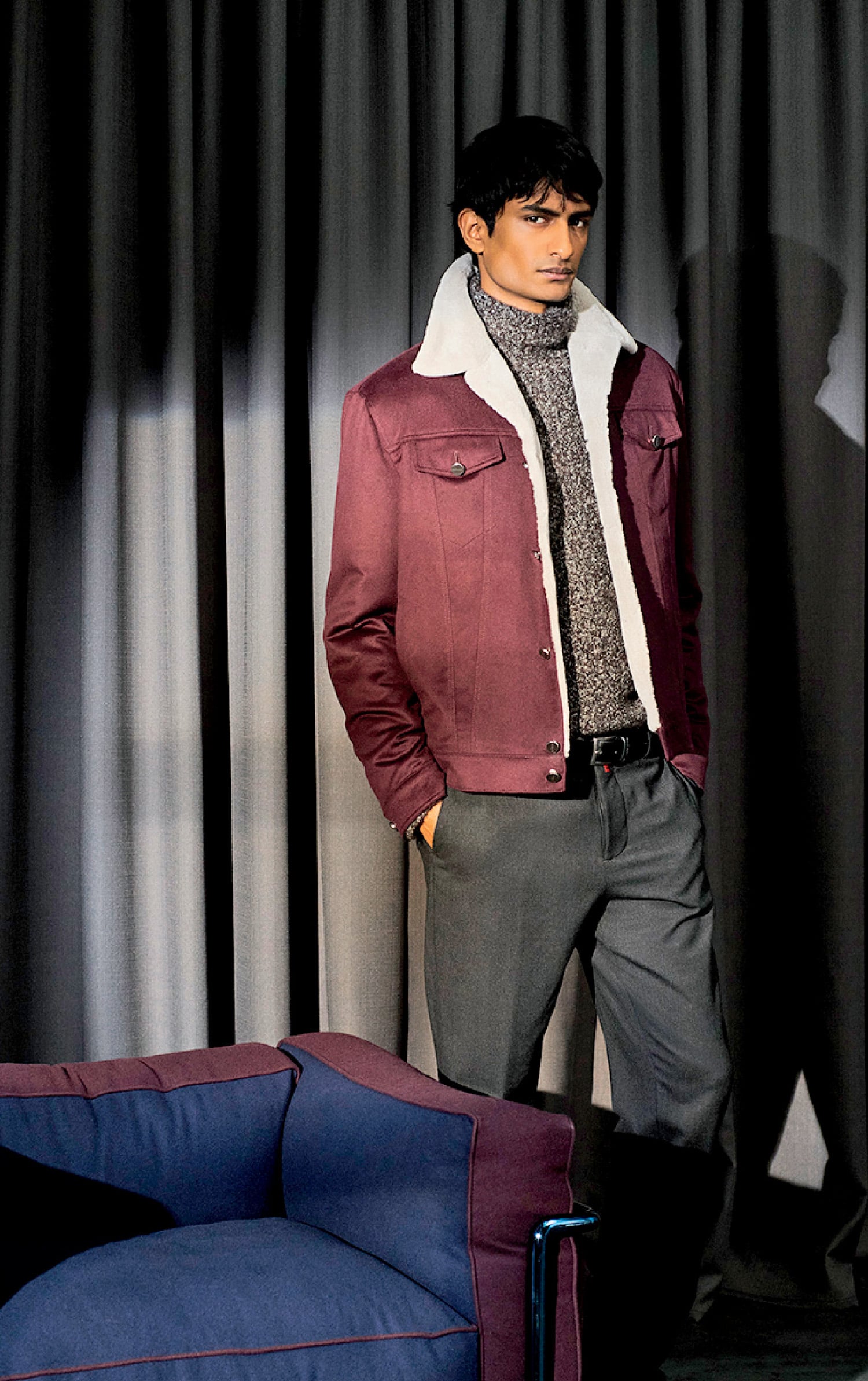 A man in a jacket and tie standing in front of a couch