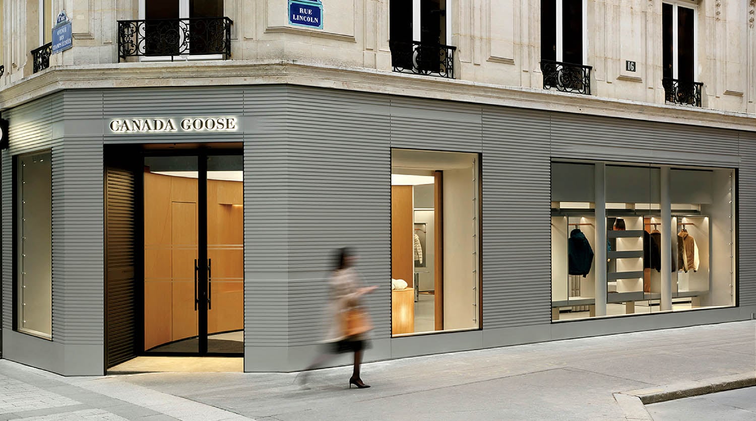 A person walking past a store with a clock.