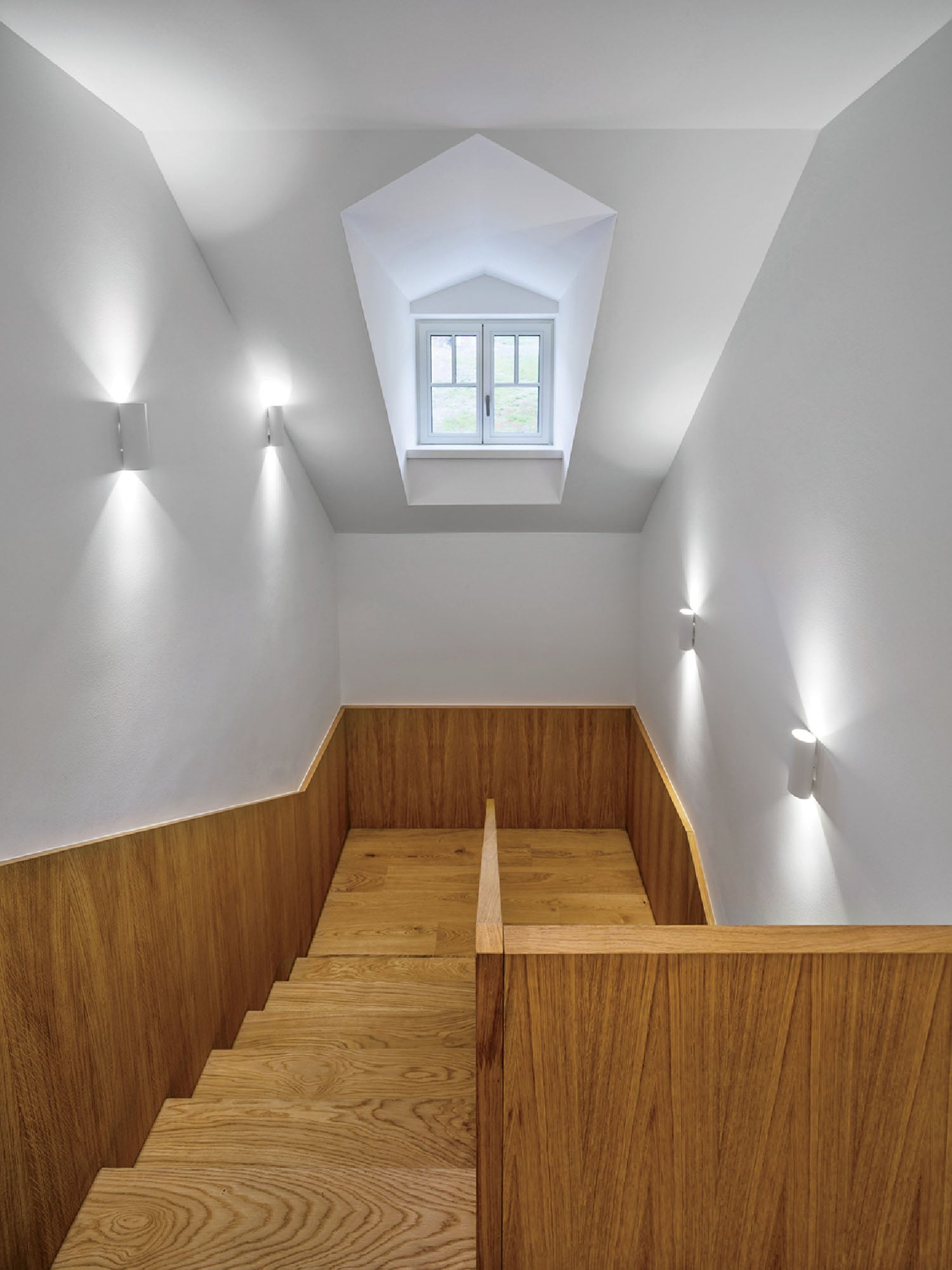 A wooden staircase with a skylight above.